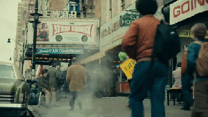 Joker - Arthur is dressed as a clown. His face is painted white, with red big lips and green curly wig. He wears a small hat. He is swaying from side to side and twirling a yellow sign