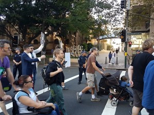 Protesters at the March for Science travel across the road. A woman in a wheelchair is seen in the foreground. A man pushing a pram is in the background