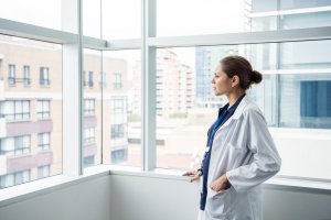 An Aboriginal woman in a white lab coat, staring out the window of an office