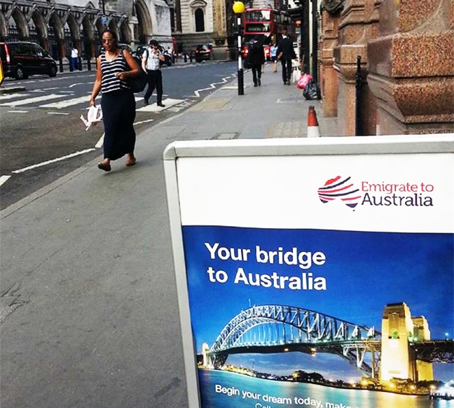 In London, emigrate to Australia sign is in the foreground, and people walk in the background