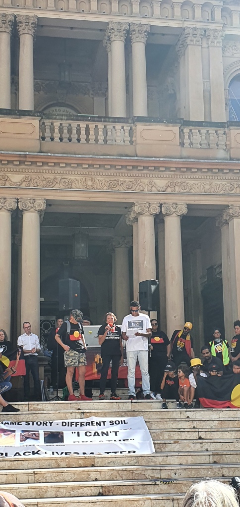 Leetona Dungay stands at the steps of Town Hall. She holds a microphone
