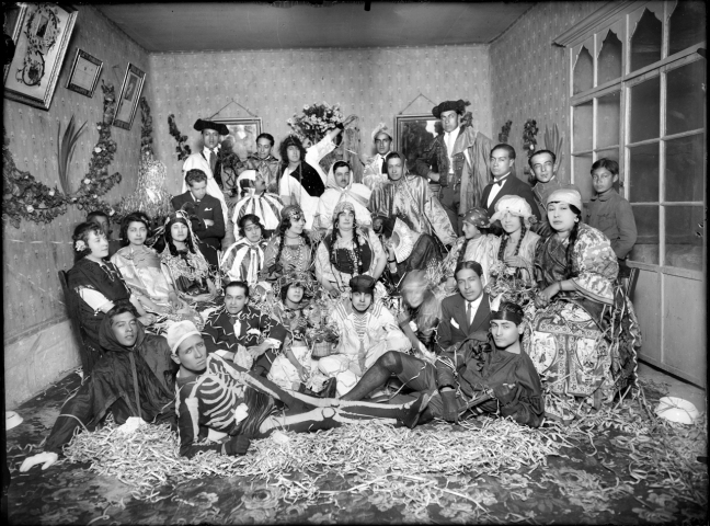 Two dozen mestizo people pose for a photo dressed in costumes. One is dressed as a skeleton