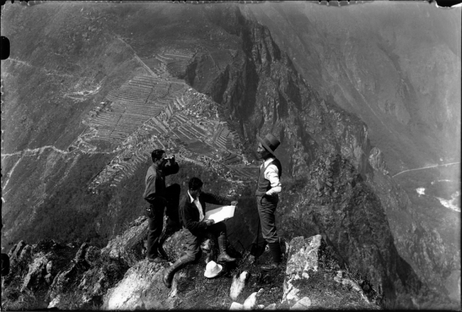 Quechuan men stand on top of a cliff, with huge mountains in the back