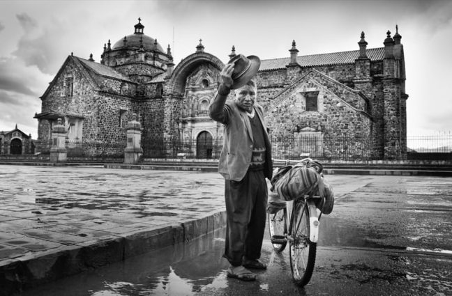 Quechuan man next to his bike. A Christian building in the background