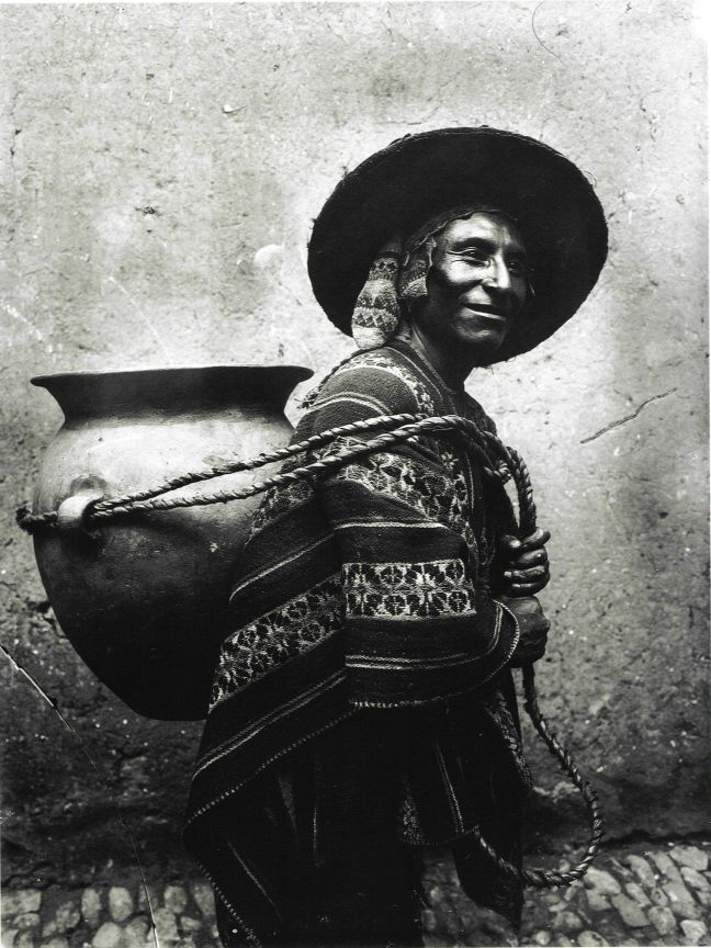 Quechuan man has a large jar strapped to his back. He is smiling