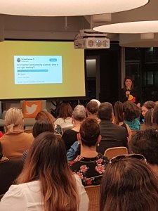 Shannan Dodson is a young Aboriginal woman. She stands in front of a large crowd beside a screen showing one of her tweets showing how to use a Twitter poll with humour