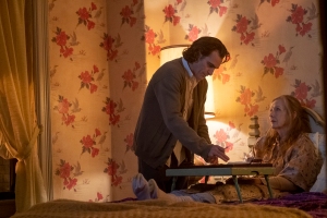 Arthur is dressed in a large cardigan. He's in Penny's bedroom, which is decorated in flowers. Penny is lying in bed. Arthur is standing over her ready to feed her