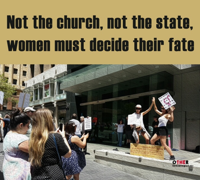 Women photograph two friends posing, who hi-five and hold a sign that can be seen distantly. It reads: Women's rights are human rights