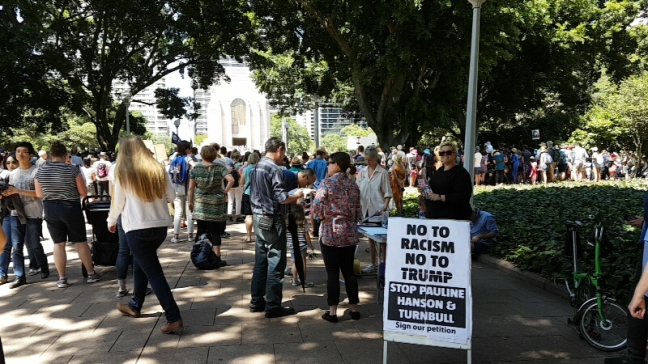 "No to racism" standing sign in the foreground with people walking in the background